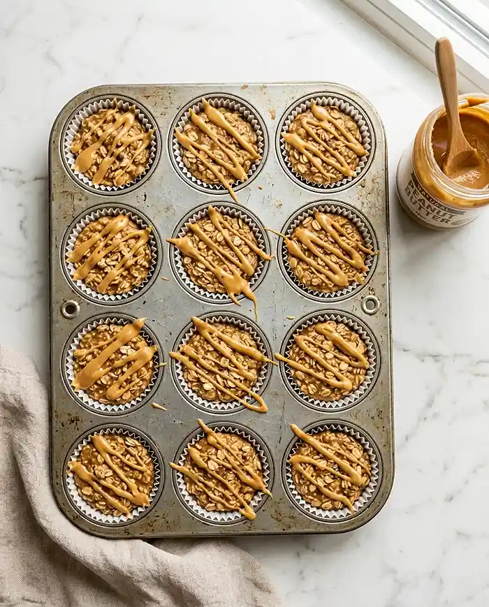 Individual no-bake peanut butter oat cups in a muffin tin with a peanut butter drizzle on top