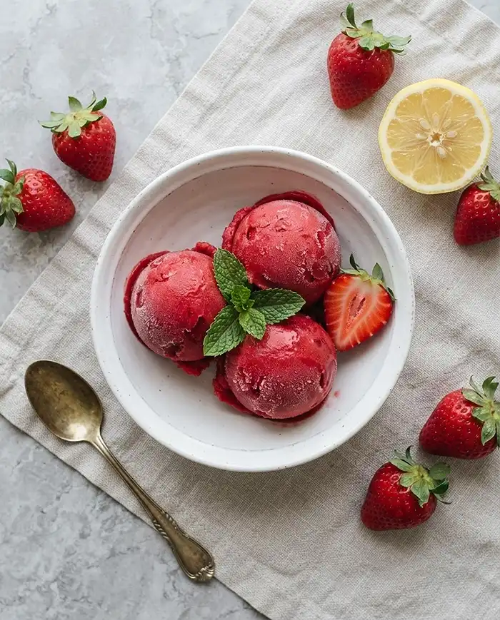 Scoops of bright red strawberry sorbet with fresh berries and mint, a classic in frozen fruit dessert recipes